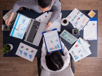 Top viewTop view of manager and employee doing teamwork in business office , looking at charts on laptop display. Finance paperwork with charts at workplace. Discusing financial plan.